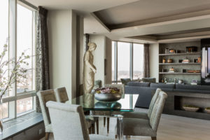 Transitional living toom, window wall, large sculpture, ceiling soffit, textured ceiling, window seat, upholsetred window bench, shared living and dining space, glass top dining table, custom millwork, built-in shelving, built-in storage, media wall, sectional, sofa console, grey, green, turquoise, open concept