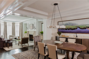 Coffered ceiling, soffit, white walls, shared living and dining space, formal dining, sitting room, transitional fireplace surround, herringbone floor pattern, oval dining table, transitional chandelier, tonal, purple accent color, oversized landscape art