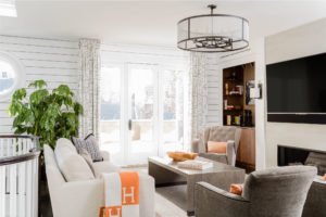 transitional media room, transitional family room, as fireplace, contemporary fireplace surround, semi-flush mount ceilig light, white wall panels, horizontal wall boards, shiplap, orange accent color, punch color, media room, transitional family room, built in storage, custom millwork, dry bar, textured wallpaper, contrast welt, wall hung flat screen TV, balcony, white walls, dark floor, contrast, skylight