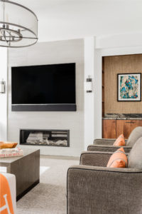 transitional media room, transitional family room, built in storage,contemporary fireplace surround,contrast,contrast welt,custom millwork,dry bar,family room,gas fireplace,horizontal wall panels,orange accent color,punch color,semi-flush mount ceilig light,textured wallpaper,wall hung flat screen TV,white wall panels,white walls