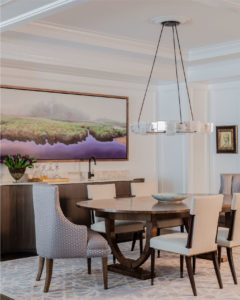 transitional dining room design, coffered ceiling, soffit, white walls, custom wet bar, custom millwork, bar sink, formal dining, oval dining table, transitional chandelier, tonal, purple accent color, oversized landscape art