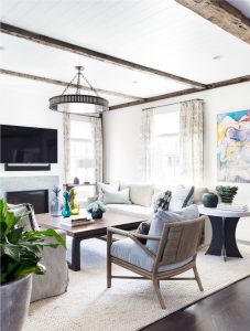 Reclaimed wood beams, decorativ beams, wallmounted television, modern rustic living room, transitional living room, wicker back lounge chair, transitional iron chandelier, colorful abstract art