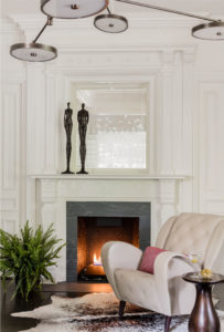 animal hide rug,applied moulding,brass sculpture,contemporary chandelier,crown moulding,fireplace surround,leather armcahir,statement chandelier,wall moulding,white walls