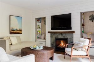 transitional media room, white ship lap walls, reading niche, built in book cases, reading nook, ratan round coffee table, transitional fireplace surround