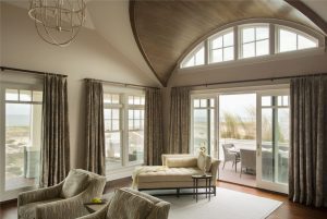 transitional living room, open living space, open concept, stained wood beams, custom drapery, transitional chandelier, chaise lounge, wood ceiling detail, sliding glass patio door, ocean view, subtle beach theme living room, neutral color palatte, arched ceilings, demilune window