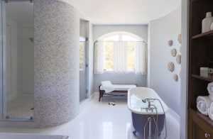 transitional bathroom, freestranding tub, soaking tub, curved bathroom walls, blue bathtub, recessed bathroom lighting, contemporary shower controls, handheld shower, dressing bench