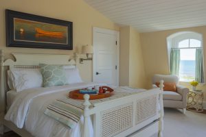 transitional beach house bedroom, yellow bedroom, ocean view bedroom, subtle beach theme design, white shiplap ceiling, French cane bed frame