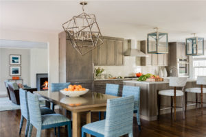 Blue dining chairs, upholstered dining chairs,contemporary fireplace surround, geometric pendant light, kitchen island, large pendant light, oversized lantern pendants, stainless steel range hood, statement lighting, transitional kitchen
