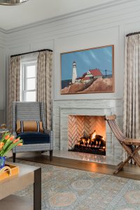 fireplace, stone fireplace, marble fireplace, oceanside artwork, high back lounge chair, decorative pillow, lumbar pillow, transitional are rug, wood paneling, white walls, curtain panels