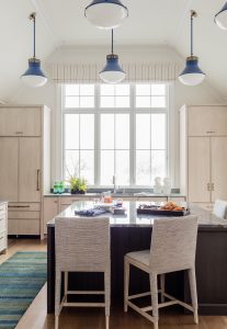 large kitchen window, roman valance, light wood cabinetry, blue ceiling pendants, rug runner, upholstered counter stools, center island, blue ceasar stone counter top, dark wood island