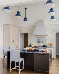 ceiling pendants, kitchen, blue ceiling pendants, blue ceasar stone counter top, wood center island, upholstered counter stools, modern stove hood, wall tiles, wood floor, light cabinetry, dark cabinetry