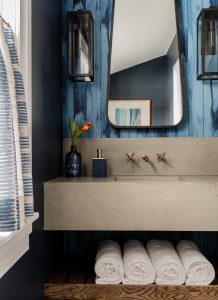 modern blue wallpaper, bue walls, bathroom, powder room, cafe curtain, stone sink, sconces, large mirror, pops of blue