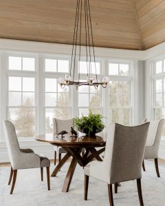 round dining table, round chandelier, area rug, dining chairs, upholstered dining chairs, area rug, wood paneling, room with many windows, wood floor