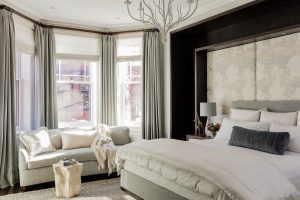 bedroom, mater bedroom, side table, nightstand, night table, table lamp, wallpaper, upholstered wall, upholstered headboard, upholstered bed, upholstered end of bed, bed pillows, bedding, bay window, floor to ceiling drapery, white chandelier, romantic chandelier, settee, small sofa,